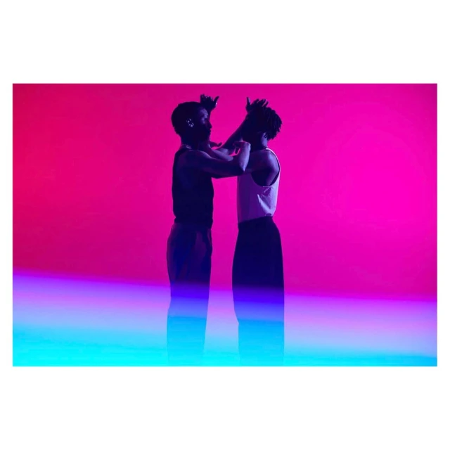 Two adults strike a pose in a studio with magenta and cyan lighting. The figures are silhouetted against a vibrant, gradient backdrop.