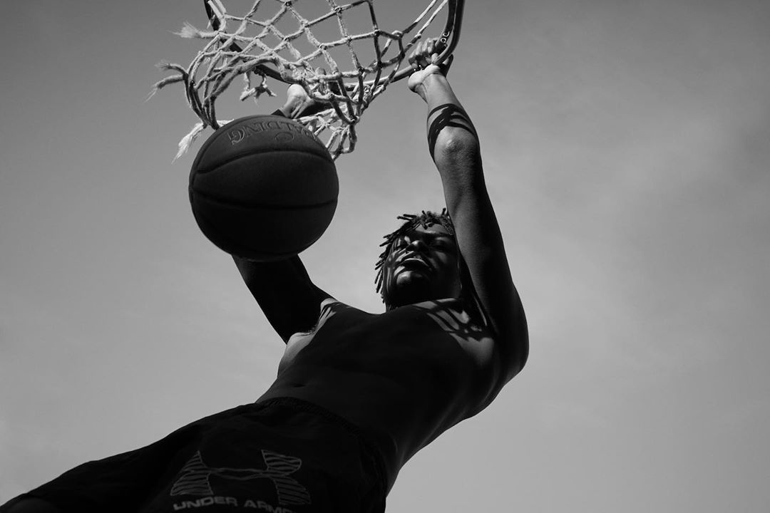 Low-angle shot of an African American man dunking a basketball into a net against a sky background, captured in black and white.