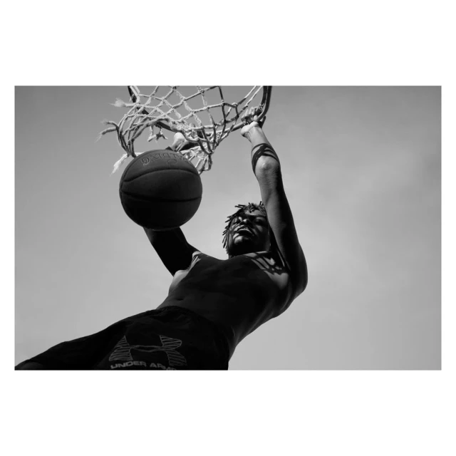 Black and white low angle of athletic male dunking a basketball into a net. The sky is the backdrop for this sports image.