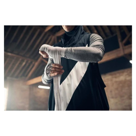 An athlete wearing a hijab and athletic apparel wraps her hands with white bandages in an indoor, industrial-style training space.