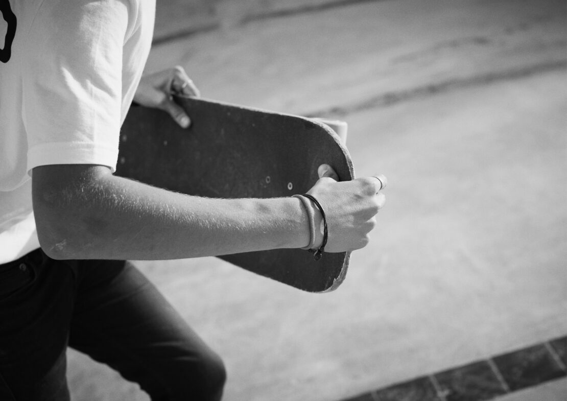 Monochrome shot of a person holding a skateboard in a skatepark, showcasing the person's arms and the skateboard's texture.