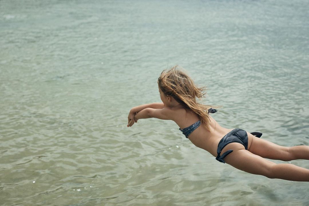 A young girl in a swimsuit dives into clear water, showcasing her form and the serene aquatic environment, capturing an active moment.