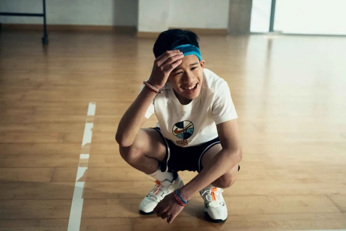 Young athlete in a white t-shirt and blue headband squatting on a wooden floor in a gymnasium by Olly Burn
