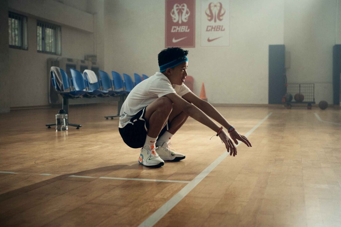 Adult man in black athletic wear sitting on a stool in a fitness studio against a black background.