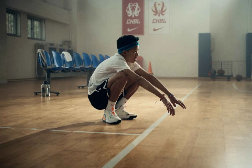 Adult man in black athletic wear sitting on a stool in a fitness studio against a black background.