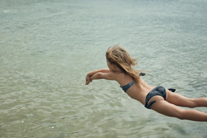 Young child diving headfirst into calm water wearing a dark patterned bikini, captured mid-air by photographer Olly Burn.