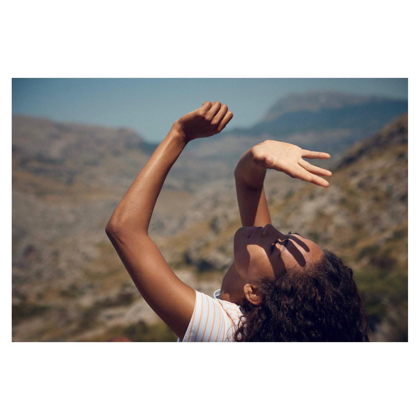 Close-up portrait of a person raising hands to cast shadows on their face outdoors against mountain hills