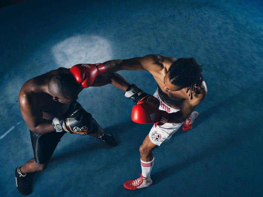 Two male boxers exchange punches in a boxing ring, captured from an overhead perspective, highlighting their intense physical engagement.