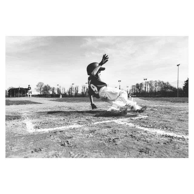 Child baseball player slides into base, monochrome shot. Action shot of young athlete in uniform at a baseball field on a sunny day.