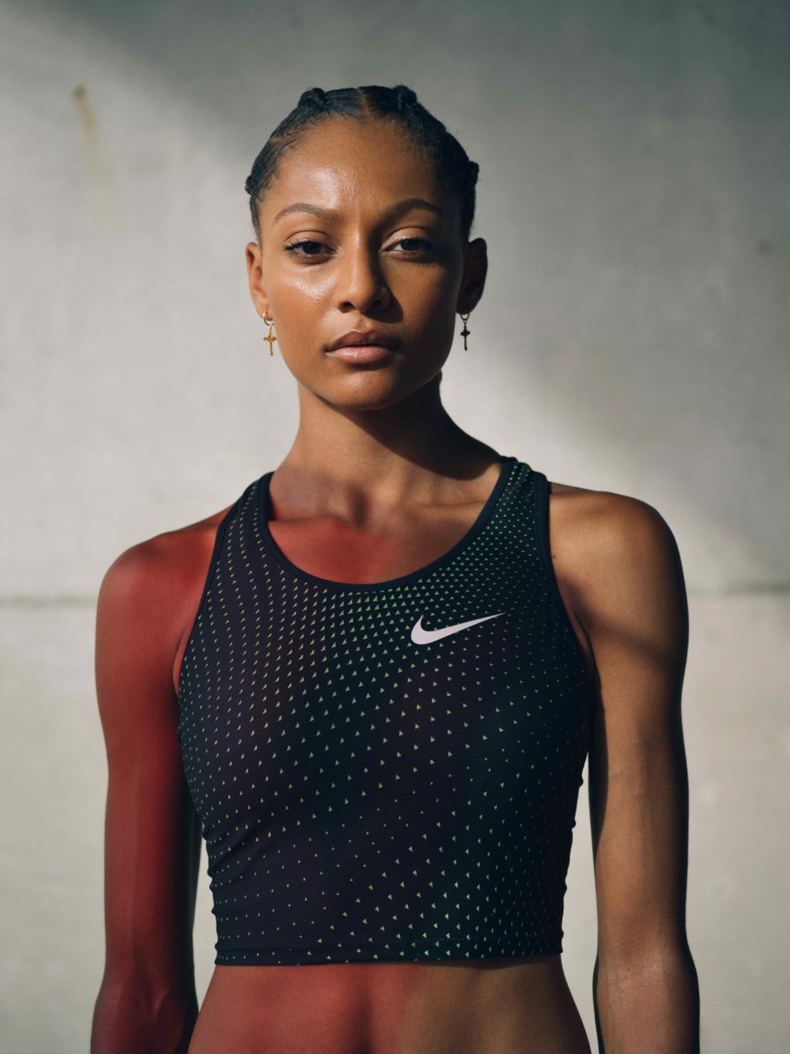 Adult female athlete in fitness apparel poses in a medium shot against a textured concrete backdrop, lit with natural light.