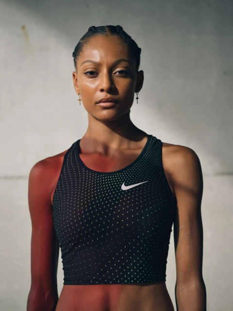 Adult female athlete in fitness apparel poses in a medium shot against a textured concrete backdrop, lit with natural light.