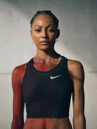 Adult female athlete in fitness apparel poses in a medium shot against a textured concrete backdrop, lit with natural light.