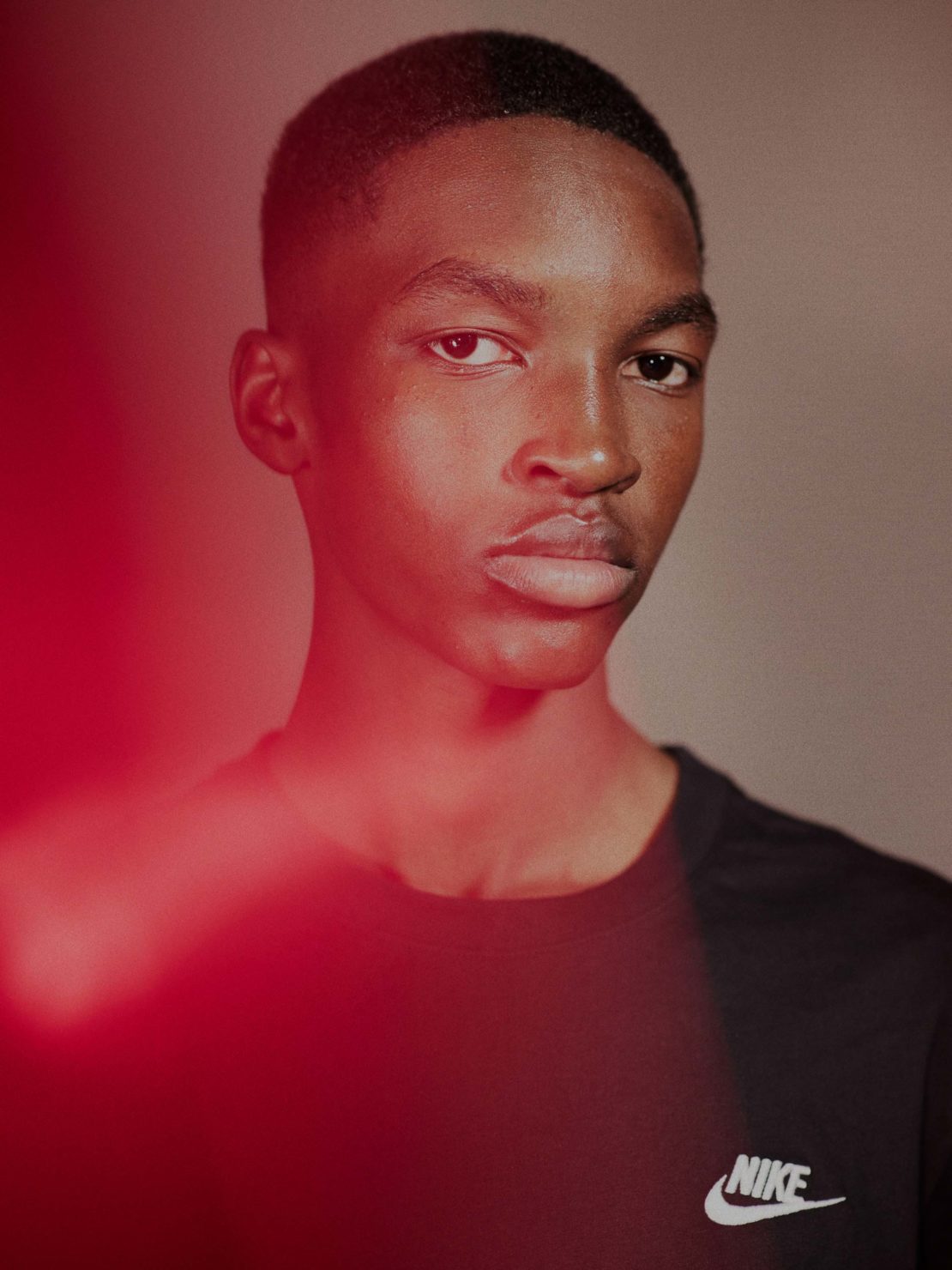 Close-up of a dark-skinned male wearing a black t-shirt with the Nike logo, featuring shallow depth of field and red light effects.