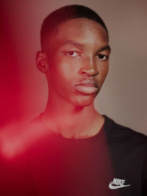 Close-up of a dark-skinned male wearing a black t-shirt with the Nike logo, featuring shallow depth of field and red light effects.