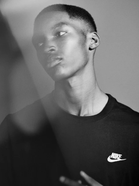 Black and white portrait of an African American adult male wearing a t-shirt with a visible Nike logo, with a light flare.