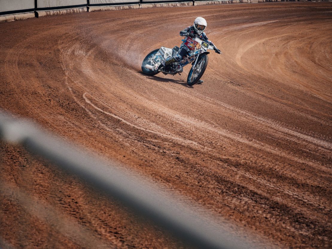 Dirt track motorcycle racer sliding through a corner on an oval dirt track kicked up dust visible