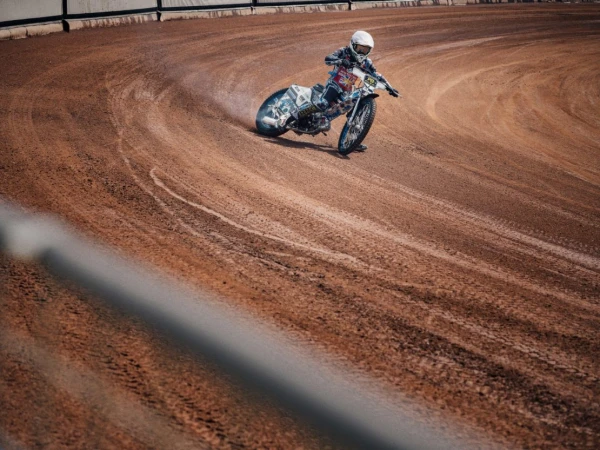 Dirt track motorcycle racer sliding through a corner on an oval dirt track kicked up dust visible