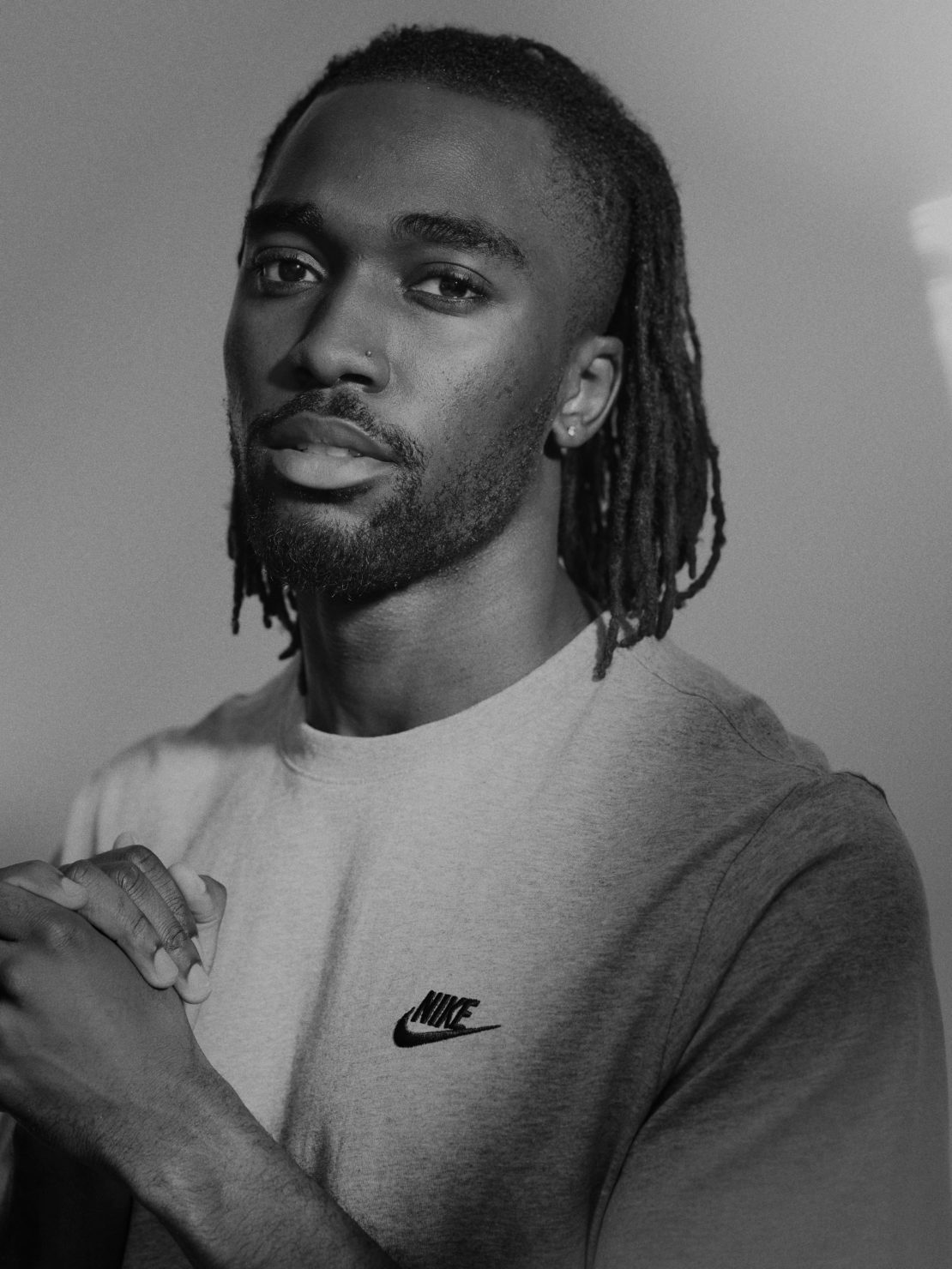 Black man with dreadlocks wearing a Nike t-shirt photographed in monochrome portrait by Paul Calver