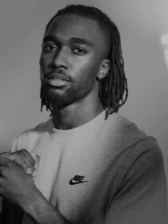 Black man with dreadlocks wearing a Nike t-shirt photographed in monochrome portrait by Paul Calver