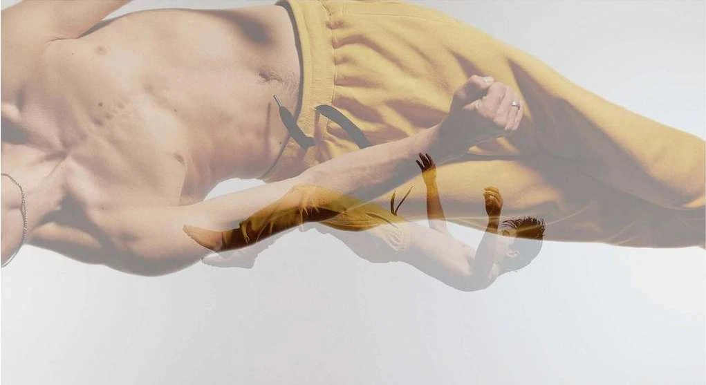 Topless man in yellow sweatpants lies in a white photo studio, double-exposed with a ghostly image for visual effects and style.