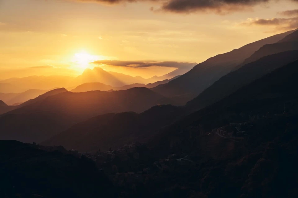 Golden sunset over a mountain range. Layers of mountains create depth, while the sun's rays illuminate the landscape and sky.
