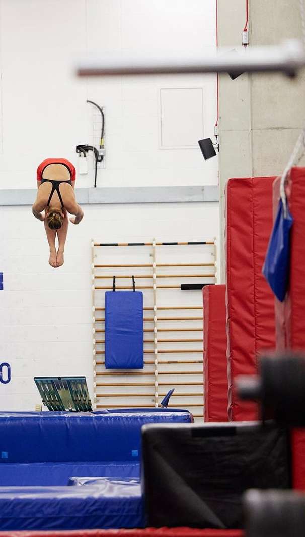 Female athlete in red swimsuit dives into a pool at an indoor training facility, focusing on the diving action and pool environment.