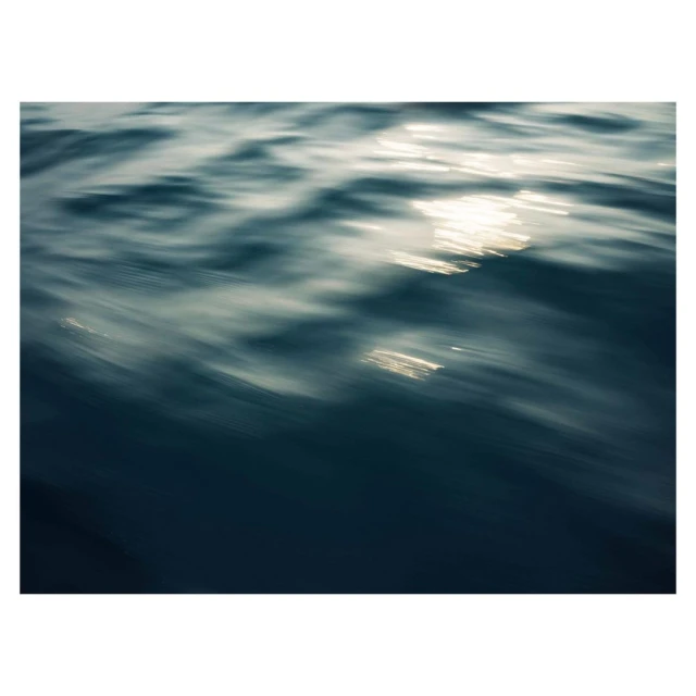 Sunlight reflects on dark blue ocean water with long exposure, creating a textured pattern of light and motion across the surface.