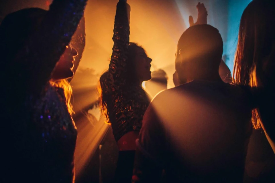 People dance in a nightclub with disco lighting, seen at a low angle under golden light.