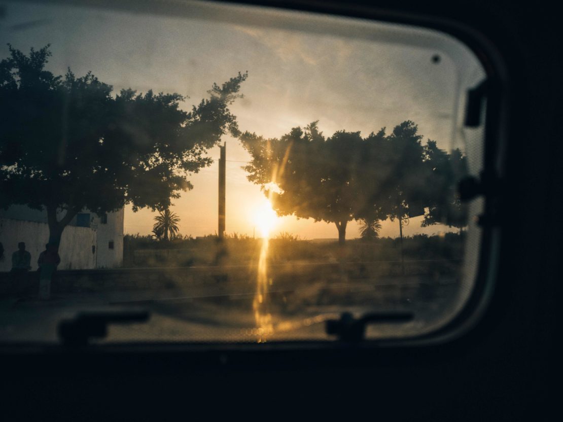 Tranquil evening view through a window of a landscape with trees, foliage, and a building with a setting sun and hazy light.