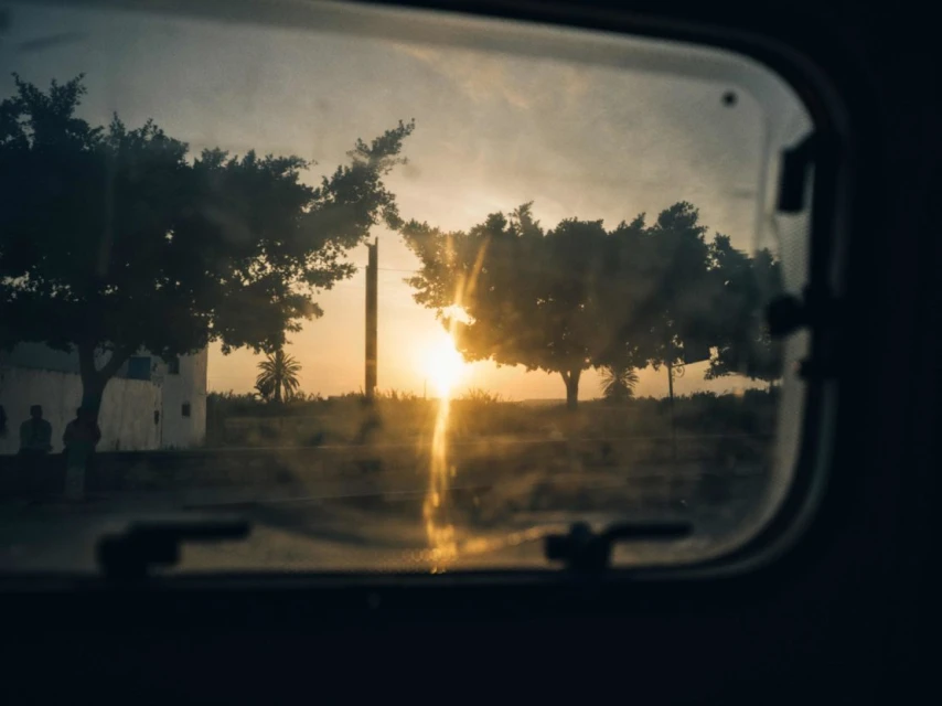 Tranquil evening view through a window of a landscape with trees, foliage, and a building with a setting sun and hazy light.