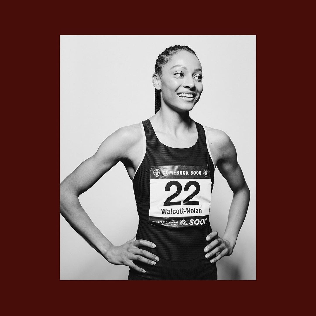 Portrait of an adult female athlete in a racing uniform, number 22, smiling and looking off to the side in a black and white studio shot.