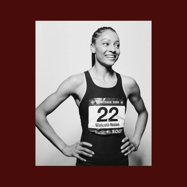 Portrait of an adult female athlete in a racing uniform, number 22, smiling and looking off to the side in a black and white studio shot.