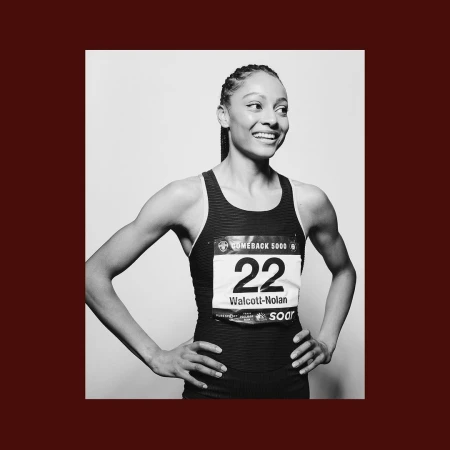 Portrait of an adult female athlete in a racing uniform, number 22, smiling and looking off to the side in a black and white studio shot.