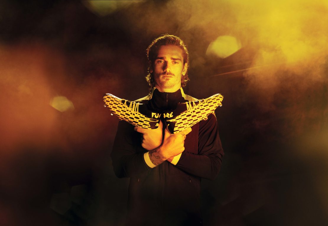 Man in black top holds soccer shoes in a studio with gold lighting, creating a dynamic and eye-catching athletic fashion image.