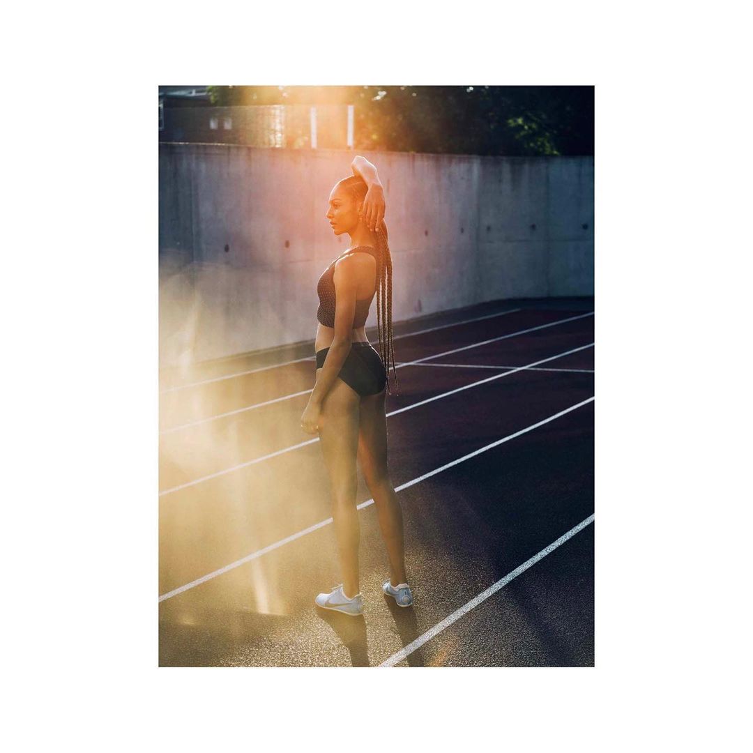 Female athlete in sportswear stands on a running track with sunlight. Outdoor fitness shot of an adult woman in athletic wear.