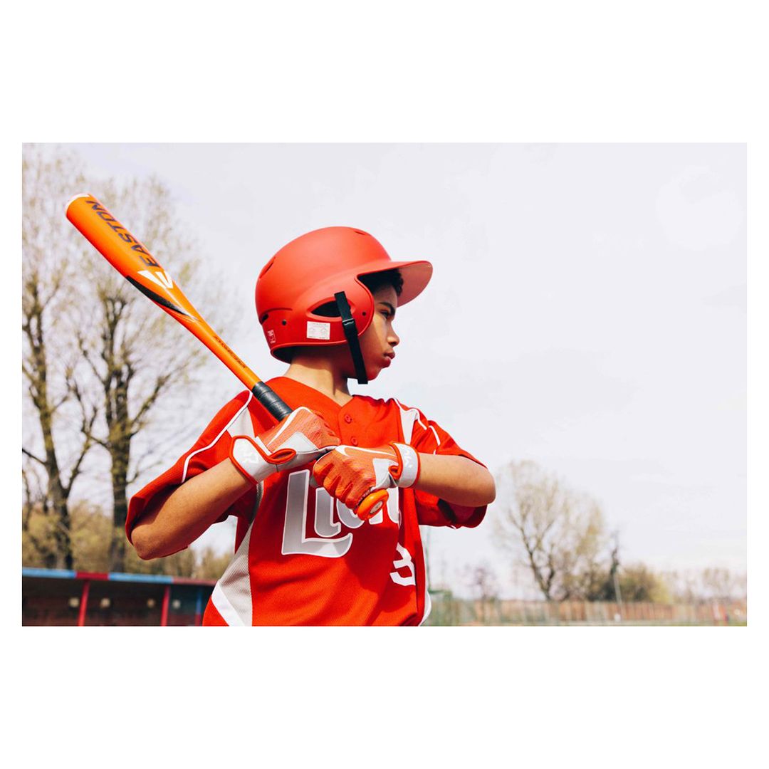 Young boy in red baseball uniform with bat and helmet prepares to bat on a sunny day in an outdoor field setting.