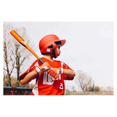 Young boy in red baseball uniform with bat and helmet prepares to bat on a sunny day in an outdoor field setting.