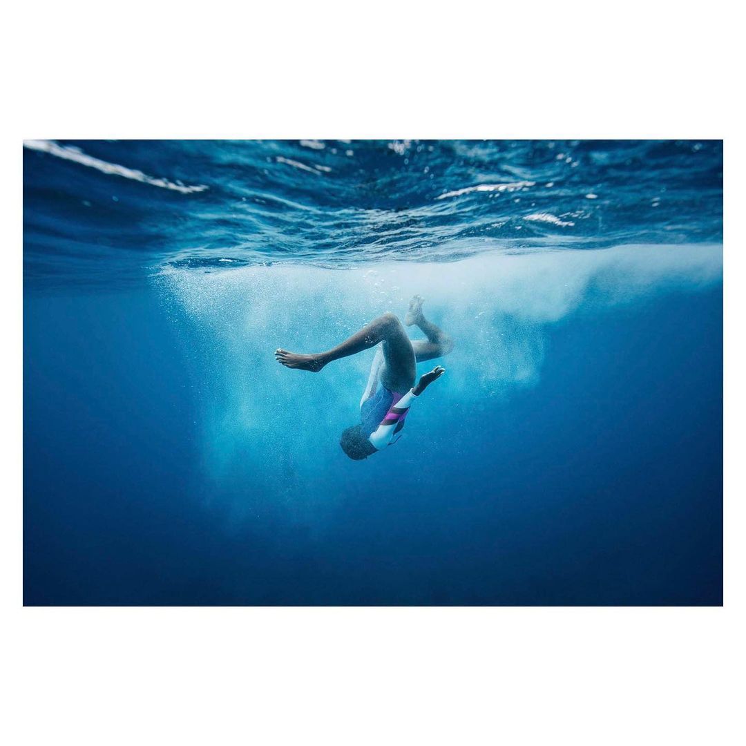 Underwater photo of an adult in a pool, showing the person falling through the water towards the depths, creating air bubbles.