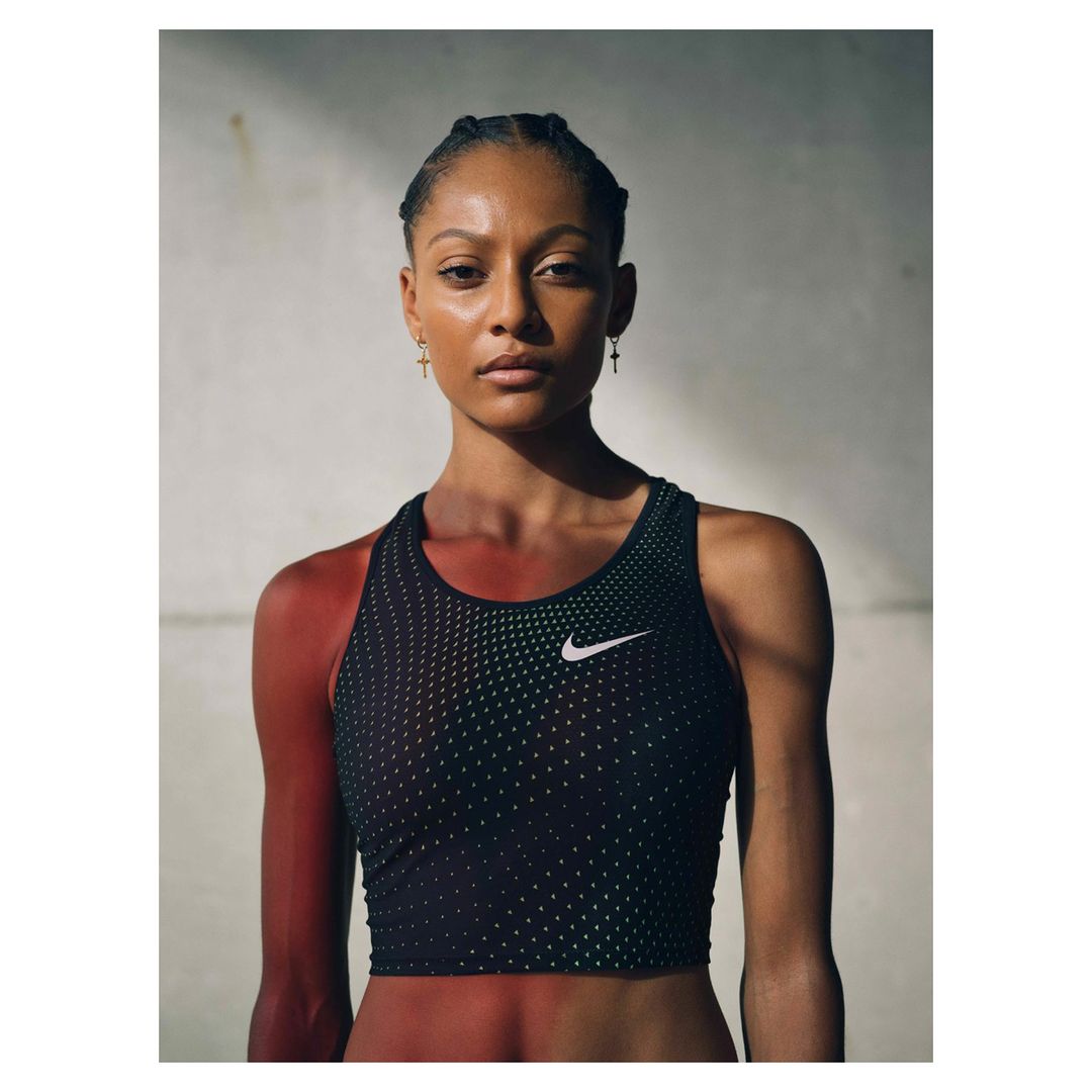 Portrait of an athletic woman wearing a black Nike sports bra with a serious expression, photographed in a photo studio with diffused lighting.