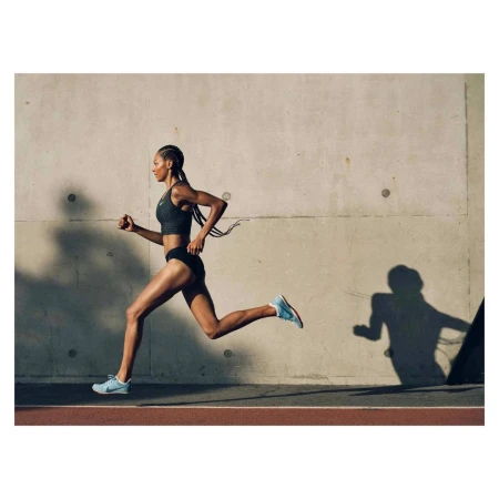 Black female runner in dark athletic crop top and shorts running past a concrete wall in London by Paul Calver