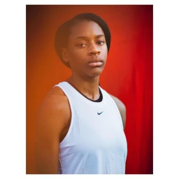 Portrait of a Black woman in a white tank top against a warm red and orange gradient background, photographed by Paul Calver.
