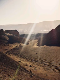 A dramatic landscape view of a desert valley between rocky hills with bright sunbeams piercing through a hazy sky, captured by Paul Calver.