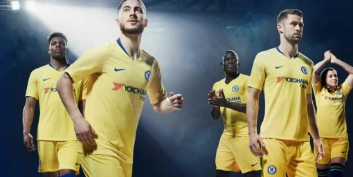 Group of soccer players wearing yellow kits standing against a dark smoky background with dramatic lighting.