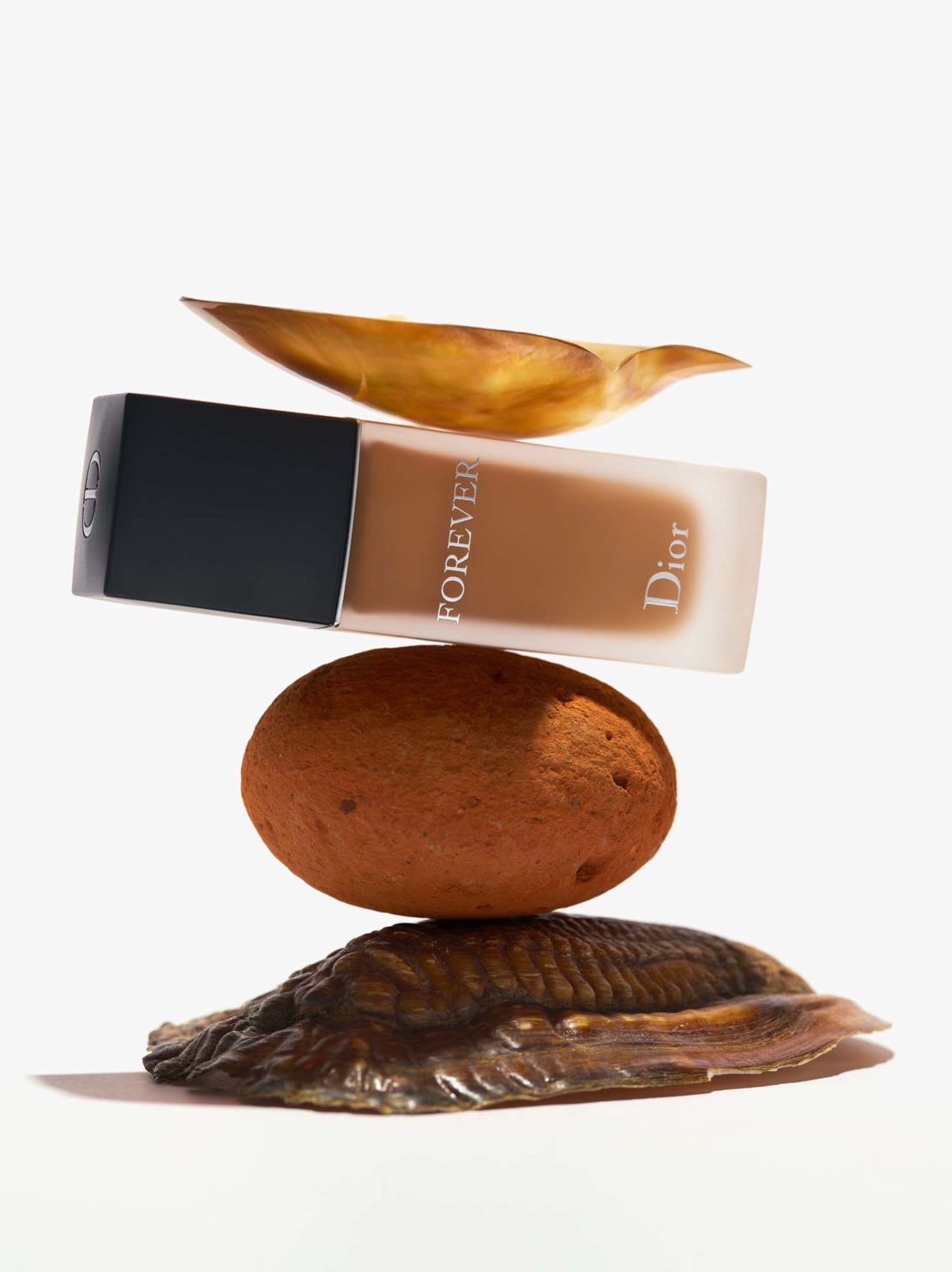 Dior Forever foundation bottle displayed with a balanced arrangement of stones and a leaf, creating a minimalist and earthy beauty product shot.