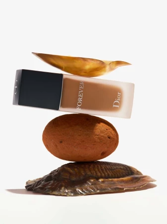 Dior Forever foundation bottle displayed with a balanced arrangement of stones and a leaf, creating a minimalist and earthy beauty product shot.