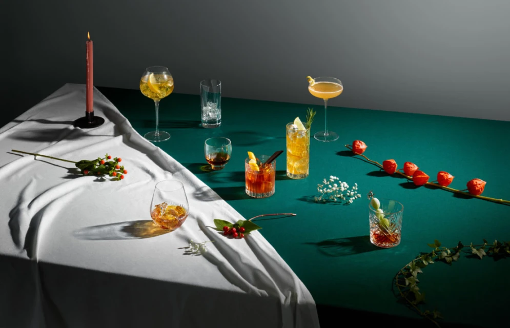 A table setup showcasing an assortment of colorful cocktails in glassware, complemented by botanical garnishes and moody, controlled lighting.