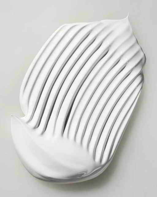 Close-up of a thick, white cream smear showing distinct ridges and a smooth texture against a soft, light gray background.