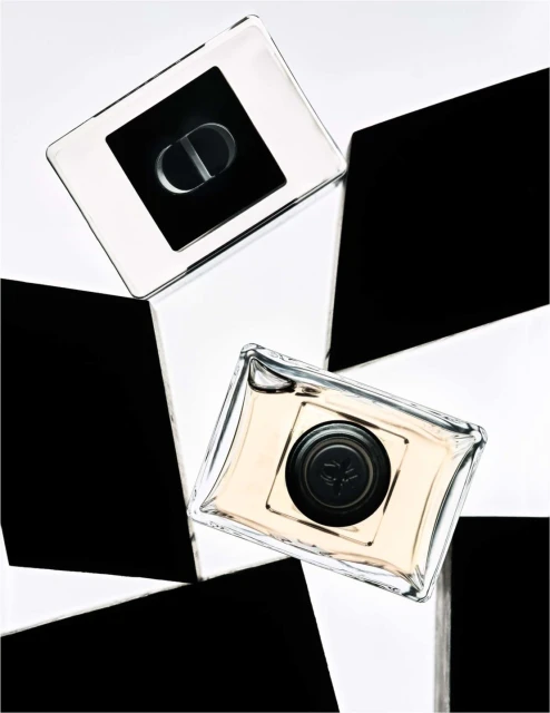 Two clear glass perfume bottles with black caps arranged on a black and white geometric surface. Luxury beauty product still life.