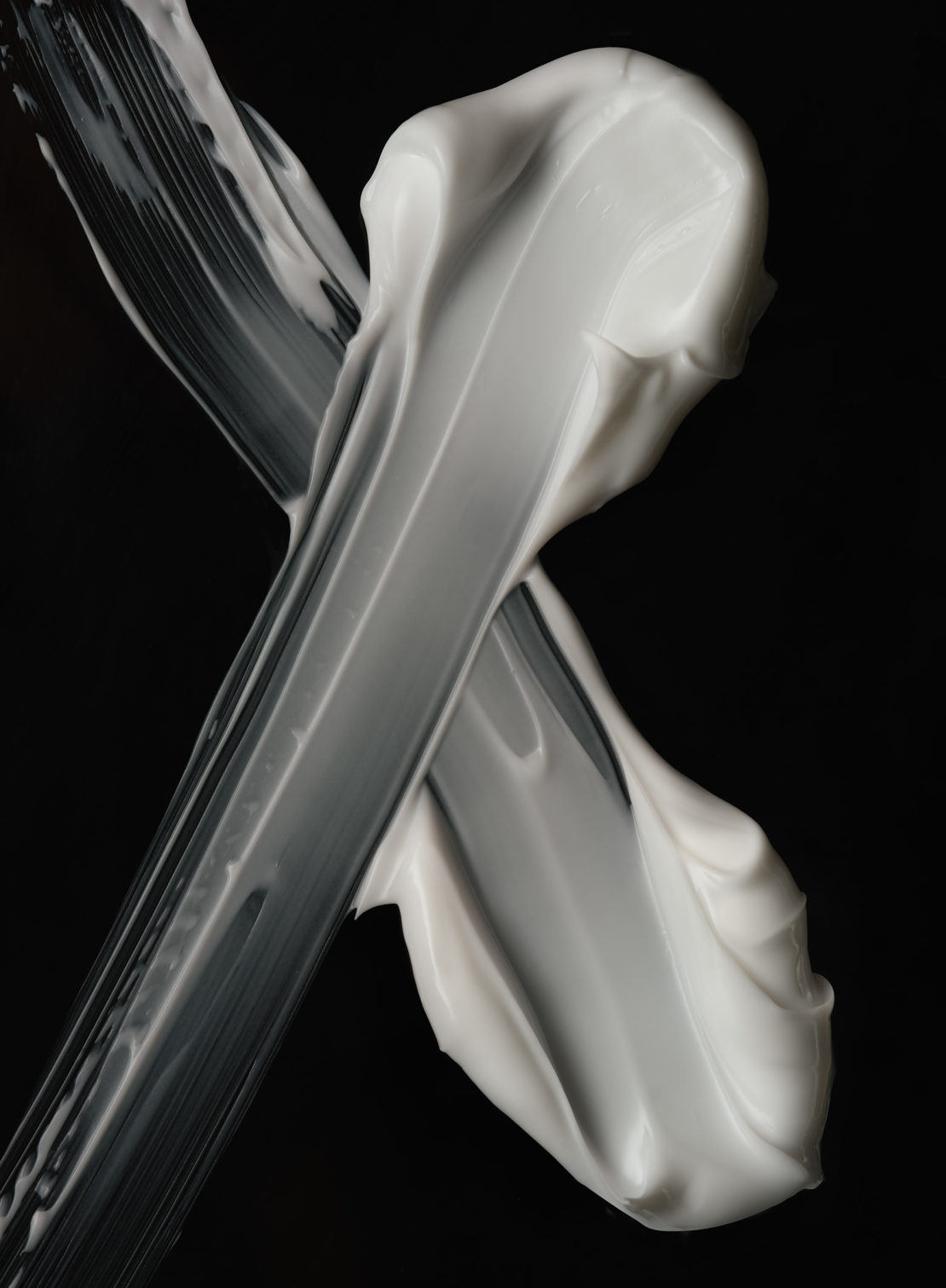 Close-up of thick smears of white cream against a stark black background creates a minimalistic and textural beauty or skincare visual.