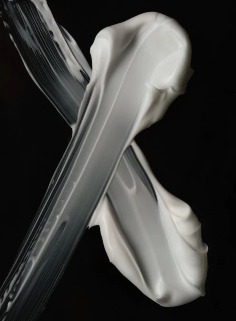 Close-up of thick smears of white cream against a stark black background creates a minimalistic and textural beauty or skincare visual.
